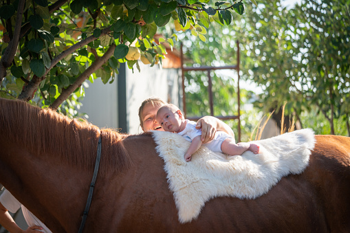 Happy mother and her newborn baby practicing horse therapy