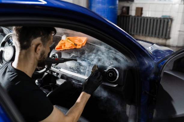 istock Foam and detergent cleaning interior in car using steam. Worker in auto cleaning service clean car inside. Car interior detailing. 1439572192