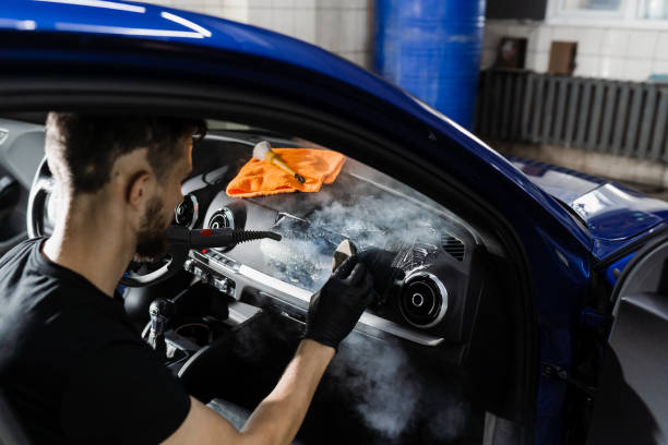 istock Foam and detergent cleaning interior in car using steam. Worker in auto cleaning service clean car inside. Car interior detailing. 1439572197