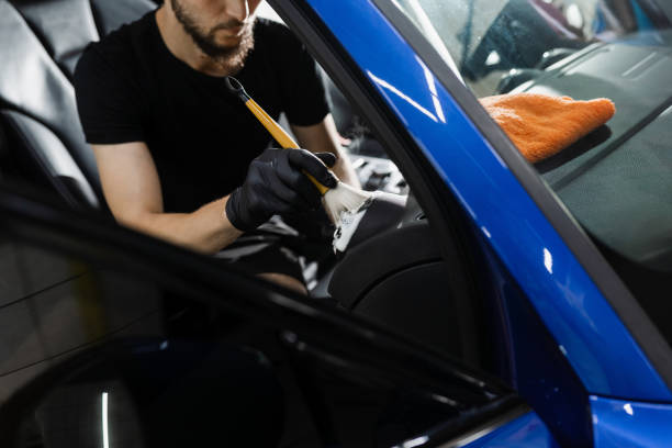 istock Car interior detailing. Foam and detergent cleaning air system using brush. Worker in auto cleaning service clean car inside. 1439572234