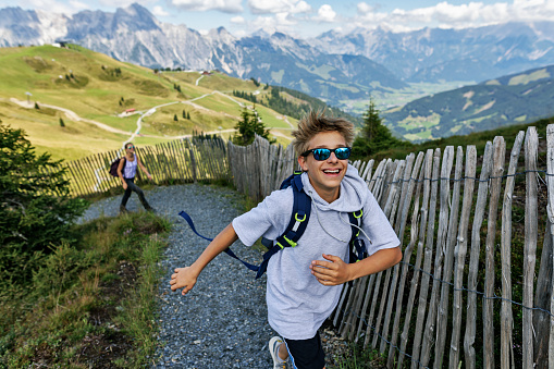 Teenage boy and teenage girl hiking in the Alps - Sazlburg, Austria. They are walking up in the mountains and looking at the view.\nCanon R5