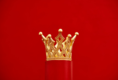 Decorative gold crown on a red plinth. Red background with copy space