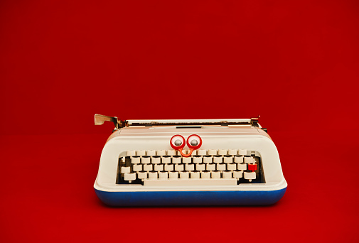 Vintage typewriter with googly eyes against a red background with space for text