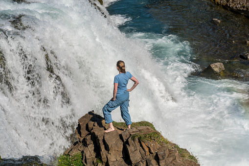 Woman standing on the rock against Rejkjafoss waterfall on sunny day, North Iceland. achievement
