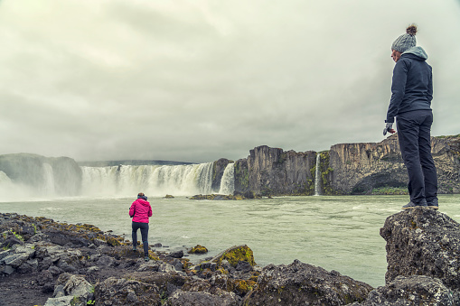 Two women walking along the Goðafoss waterfall in Northern Iceland on cloudy day