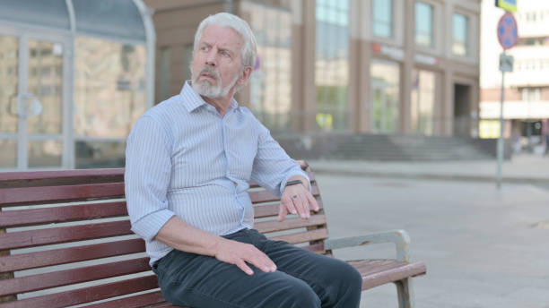 istock Waiting Old Man Checking Time on Watch while Sitting Outdoor on Bench 1439578452