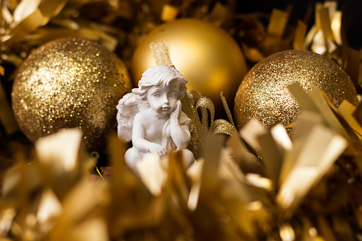Angel arround golden Christmas balls with gold tinsel on wooden background with copy space