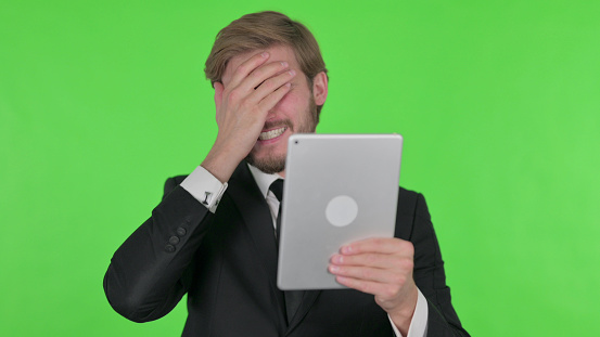 Young Adult Businessman Reacting to Loss on Tablet on Green Background