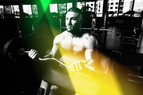 Muscular Man Doing Heavy Weight Exercise For Biceps With Barbell In Gym