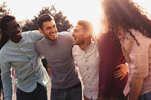 A shot of a small group of friends posing for a photo whilst spending time together at the beach in North Shields, North East England. They are smiling and two of them are raising their arms, all wearing warm clothing. It is a winter's day and the sea and quayside are visible in the background.