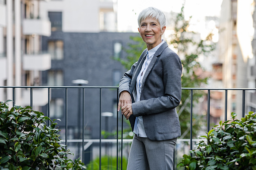 Portrait of a mature businesswoman with short gray hair. A confident female professional in elegant clothes is standing by the fence and looking at camera.