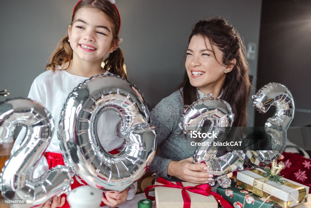 Mother and daughter holding balloons in the shape of numbers 2023. and celebrating New Year Mother and daughter are at home, they are holding 2023. balloon numbers New Year Stock Photo