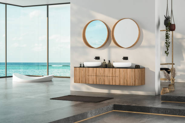 istock Modern bathroom interior with concrete floor, two sinks, double mirrors, white bathtub, interior plants, sea view from window.Minimalist bathroom with modern furniture and panoramic view. 3D rendering 1439610031