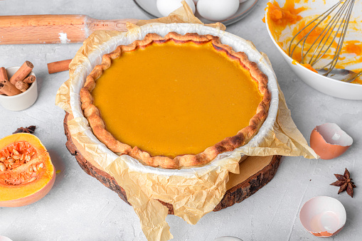Pumpkin pie into a baking dish on a gray kitchen table surrounded by ingredients. Home cooking concept, traditional thanksgiving pumpkin pie recipe, lifestyle, close up