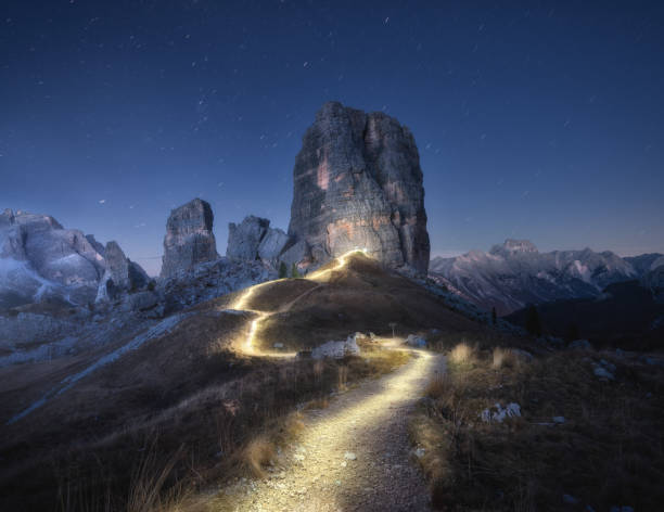 istock Flashlight trails on mountain path against high rocks at night in autumn. Dolomites, Italy. Colorful landscape with light trails, trail on the hill, alpine mountain peaks, sky with stars in fall 1439613198