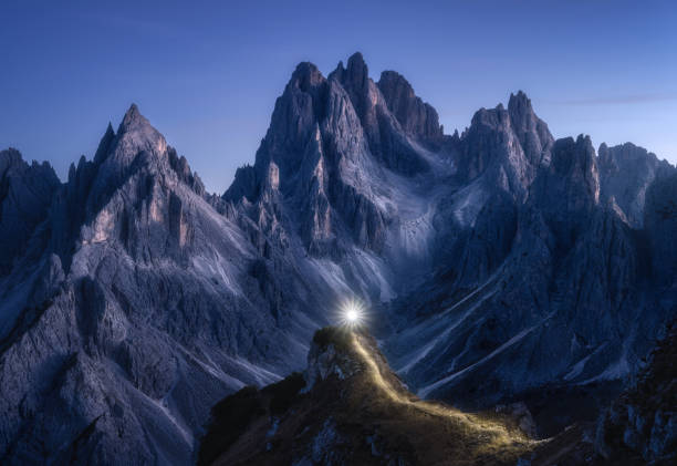 istock Flashlight trails on mountain path against high rocks at night in autumn. Tre cime, Dolomites, Italy. Colorful landscape with light trails, trail on the hill, mountain peaks, sky with stars in fall 1439613200