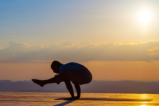 Man silhouette standing on hands, practicing firefly yoga pose. Tittibhasana, handstand asana, person outdoors workout at sunrise