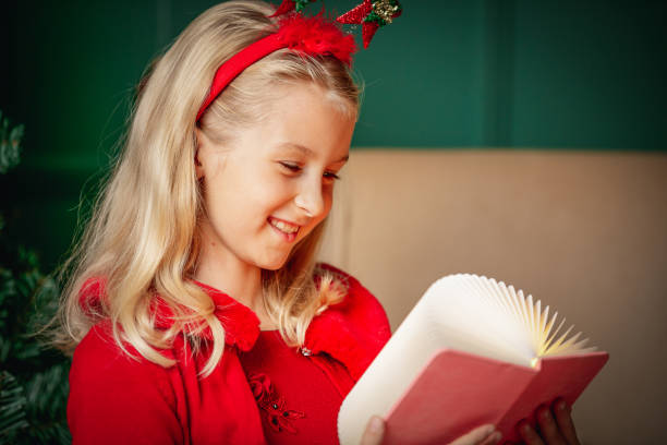 porträt eines schönen blonden mädchens in rotem kleid und stirnband, das lächelt und zur weihnachtszeit ein buch liest - 6206 stock-fotos und bilder