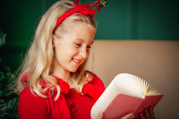 portrait of beautiful blond girl in red dress and headband smiling and reading a book at christmas time - 6206 imagens e fotografias de stock