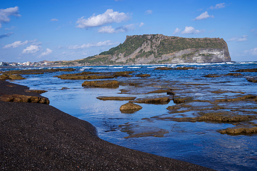 Seongsan Ilchulbong on Jeju Island, South Korea, with black sand and rocks at Gwangchigi Beach in the foreground.
