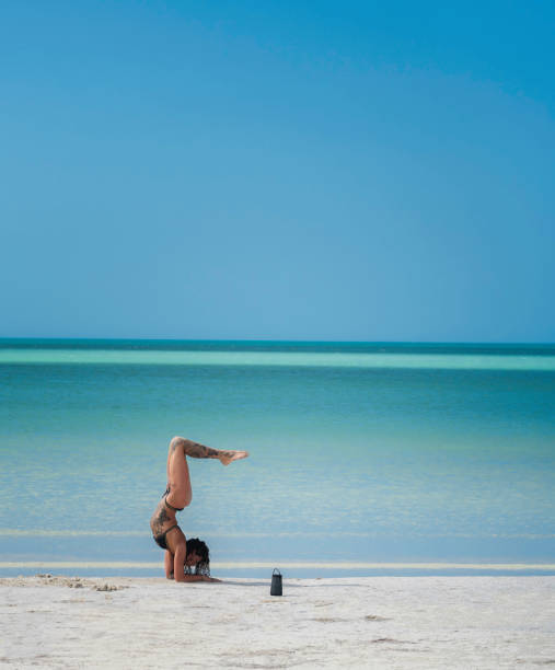 Isla Holbox, Yucatan, Mexico - April 9, 2021: A tattoed woman performs flexible yoga poses on the white sand beach at the Gulf of Mexico.