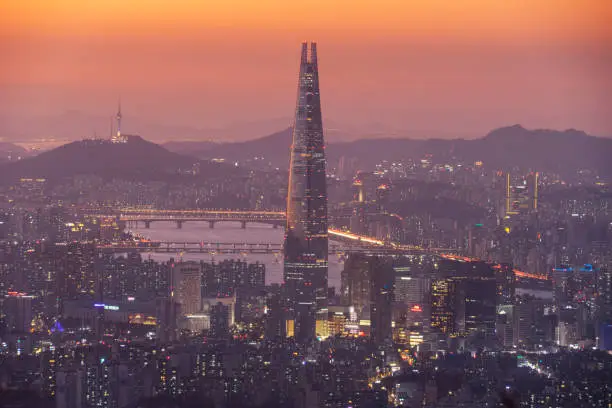Seoul skyline, seen from Namhansanseong at sunset with local landmarks like the Lotte Tower in the middle and the Han River and Namsan Tower in the background on the left.
