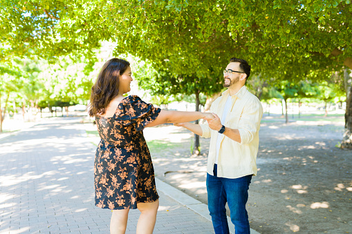 Playful beautiful couple looking in love dancing at the park and holding hands while dating