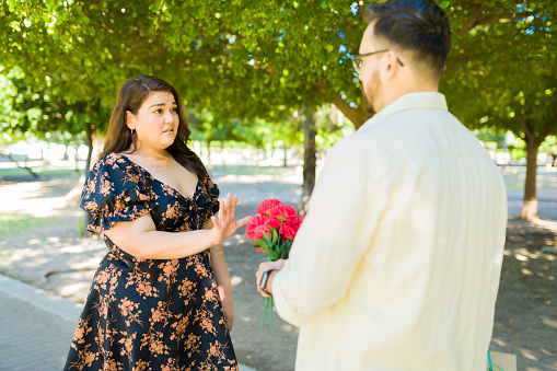 Upset hispanic woman looking annoyed while rejecting flowers and a present from her date