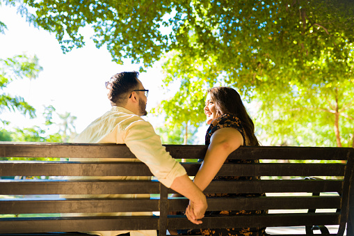 Lovely young couple holding hands while sitting together at the park bench for their date