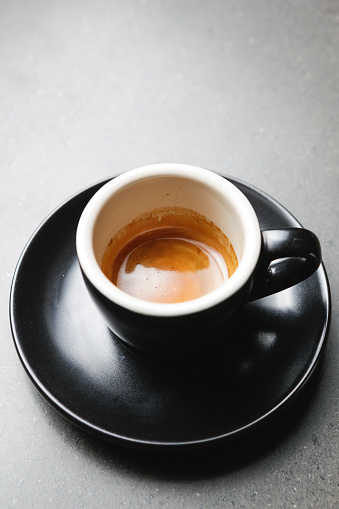 A black cup and saucer hold an espresso on a concrete bench top.