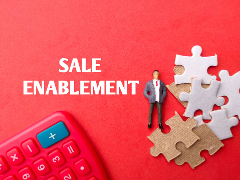 Calculator,miniture people and puzzle with text SALE ENABLEMENT on red background