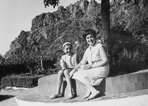 Black and white Image taken in the sixties, smiling woman and her daughter posing in the mountains