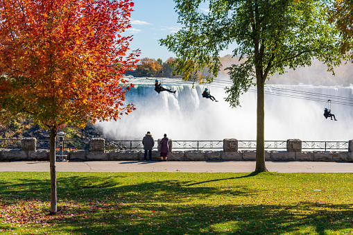 People using the Niagara Falls Zipline ride attraction. Niagara Falls City Red maple leaf during autumn foliage. Ontario, Canada.