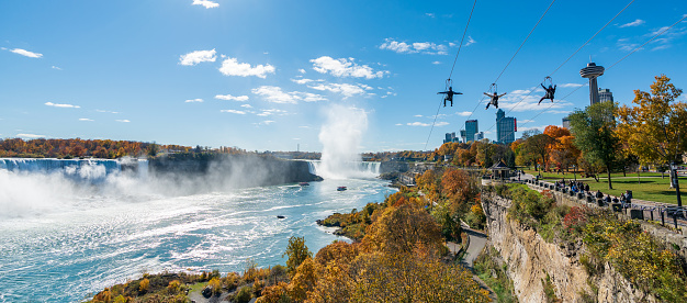 Niagara Falls City, Ontario, Canada - October 27 2022 : People using the Niagara Falls Zipline ride attraction. Red maple leaf during autumn foliage.