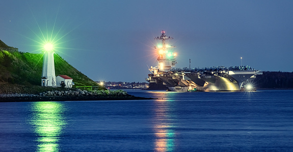 American aircraft carrier anchored in a harbour near a lighthouse after offshore training exercises.