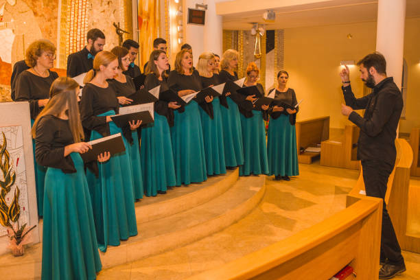 istock A large group of people dressed in the same formal clothes rehearse before a choral performance with a musical conductor 1439656512