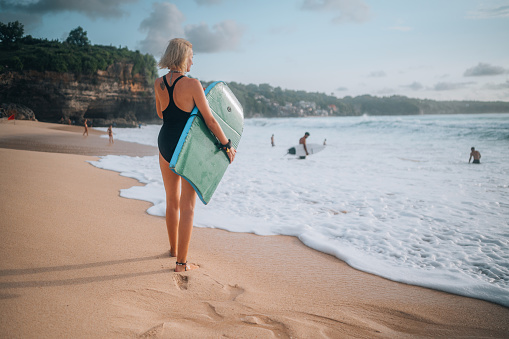 Rear view of a woman with bodyboard entering the water to catch some waves in Bali, during a beautiful sunny day.