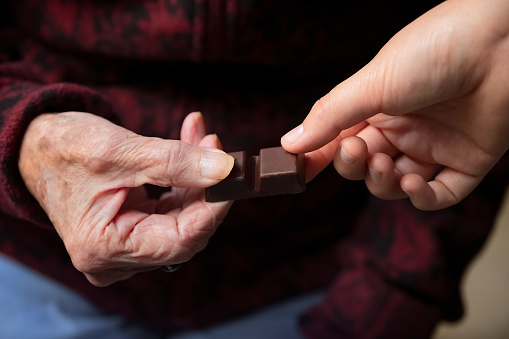 Chinese grandmother in her 90s sharing chocolate bar with Eurasian granddaughter in her 20s.  Vancouver, British Columbia, Canada.