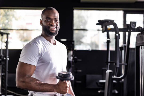 istock Fit and muscular african man doing biceps workouts with dumbbells in gym, copy space. 1439671089