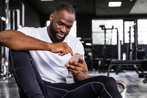 istock Sporty african man resting, looking at phone having break after doing exercise 1439673019