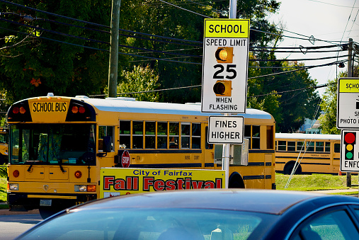 Fairfax, Virginia, USA - October 6, 2022: A Fairfax County Public Schools bus passes a flashing school speed limit sign after picking up students from W.T. Woodson High School.