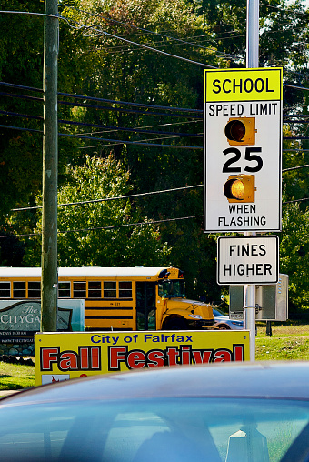 Fairfax, Virginia, USA - October 6, 2022: A Fairfax County Public Schools bus waits at a stoplight near a flashing school speed limit sign after picking up students from W.T. Woodson High School.