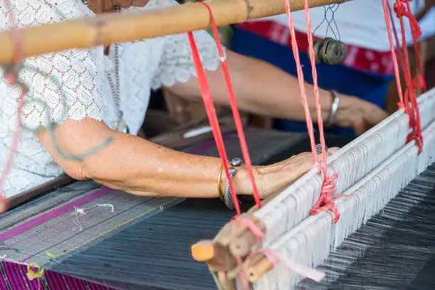 Traditional Isan Thai silk weaving. old woman hand weaving silk in traditional way at manual loom.