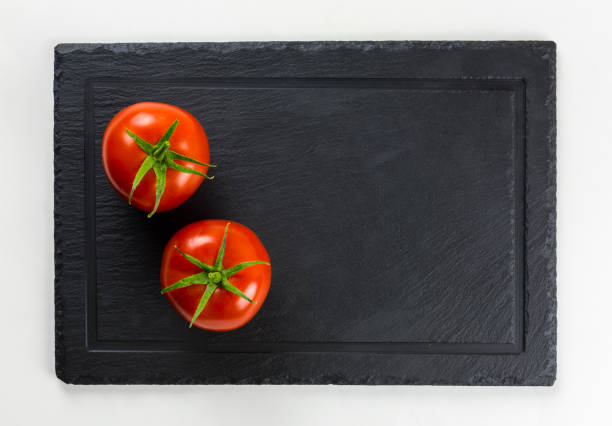 Fresh tomatoes with green leaves isolated on black serving platter.