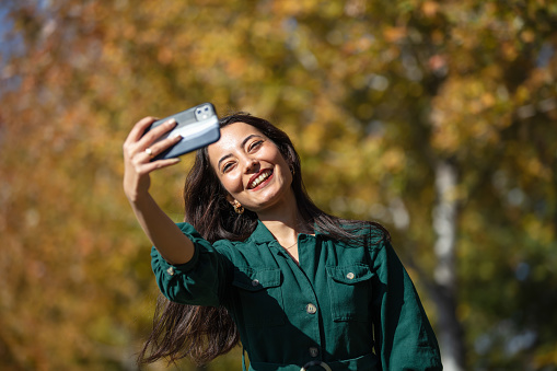 Beautiful woman in green dress taking selfie in public park. In the city of Istanbul in autumn, the parks look very beautiful in yellow.