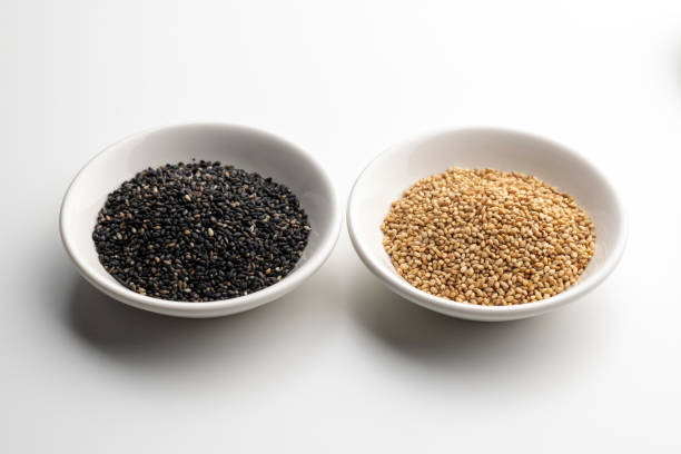 geröstete weiße und schwarze sesamsamen auf weißem hintergrund. - white sesame seed stock-fotos und bilder