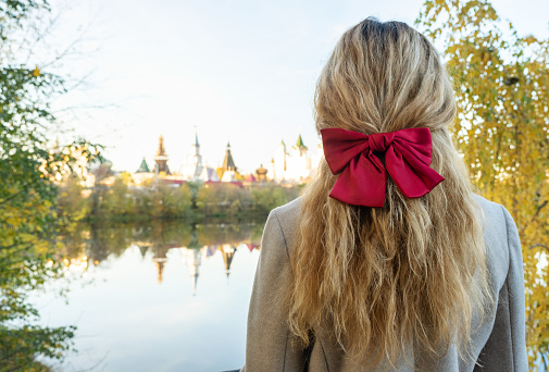 A girl with a red bow on her hair stands backwards to the camera and looks at the autumn landscape
