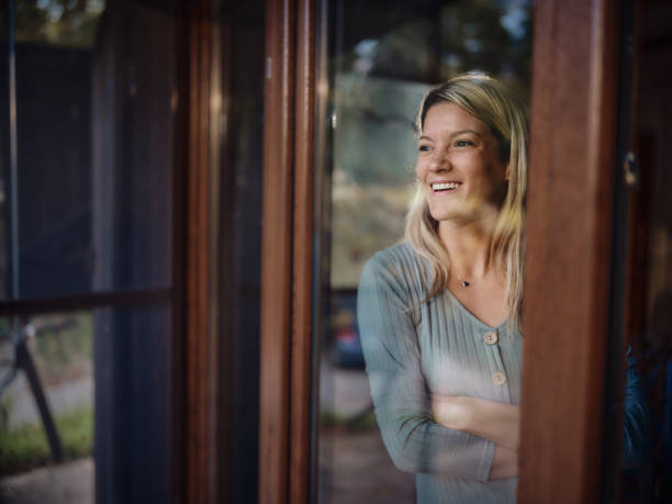 istock Happy woman looking through window from her home. 1439684701