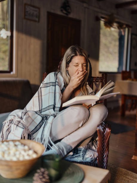 istock Woman yawning while reading a book in living room. 1439685092