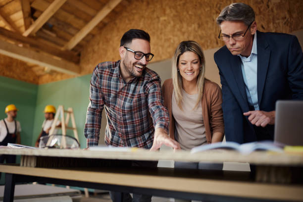 istock Happy couple going through plans with an architect at construction site. 1439685452